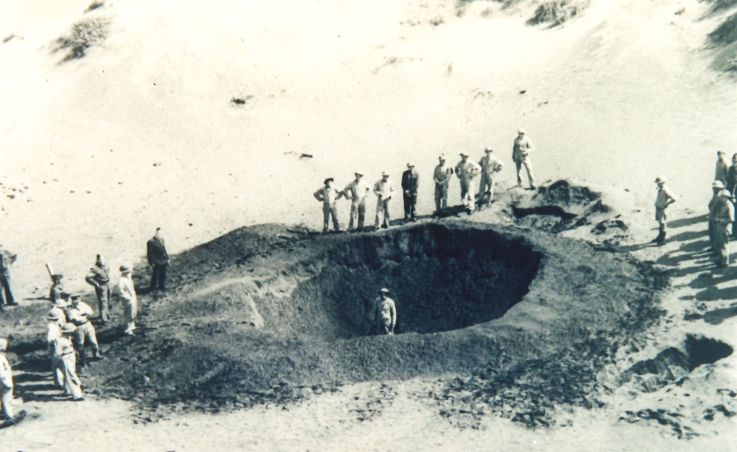 Members of 2C Section inspecting the crater formed after exploding an anti-shipping bomb at Bell Block (14 February 1943). Unknown photographer. Collection of Puke Ariki (ARC2002-10).