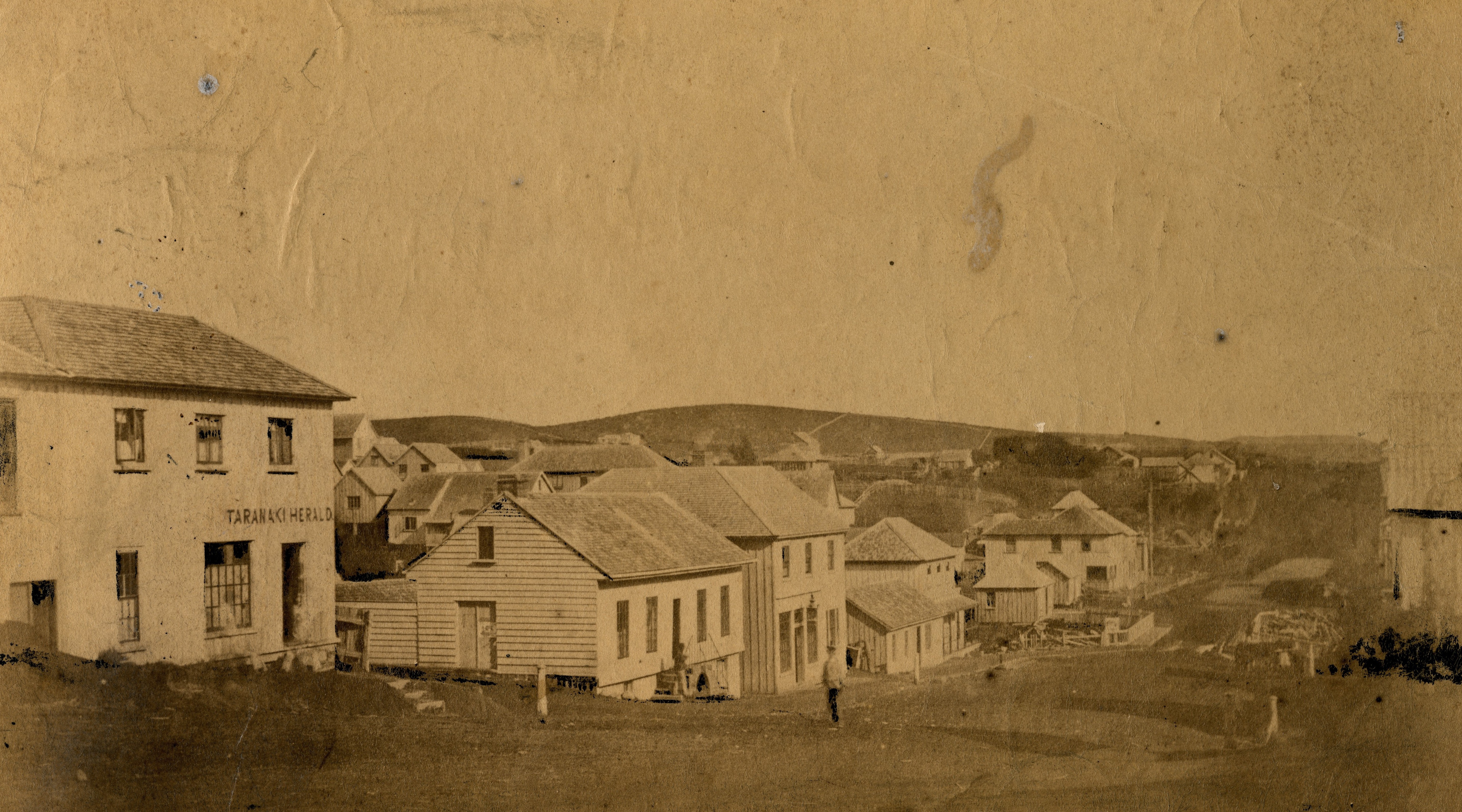 View of Devon Street near the intersection with Currie Street showing the Taranaki Herald building on the far left (1859). Hartley Webster. Collection of Puke Ariki (PHO2004-182).