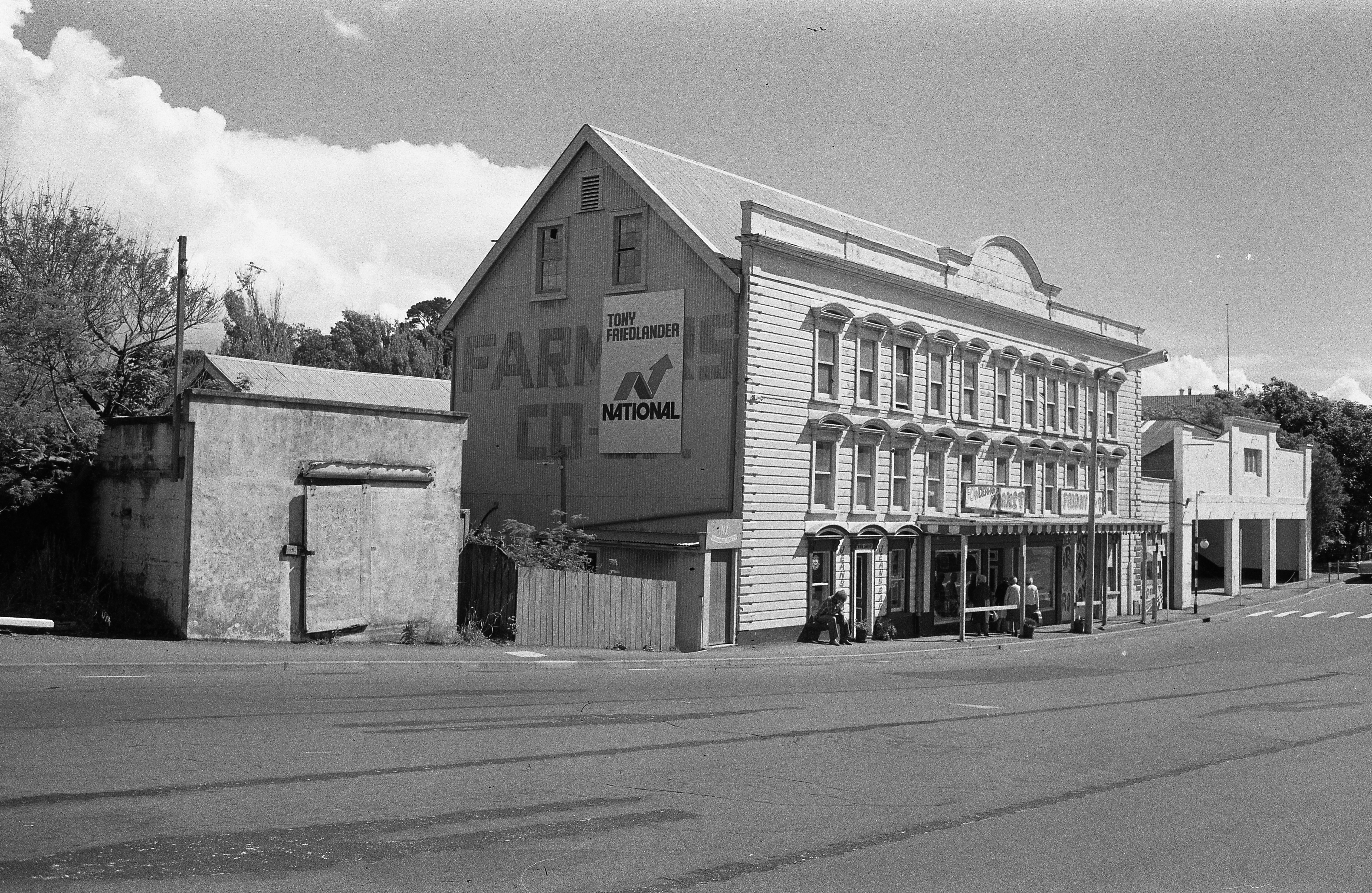 The old Egmont Steam Flour Mill with signs for the Powderham Street Market above its entrance (26 November 1976). Caleb Wyatt. Collection of Puke Ariki (PHO2012-0106).