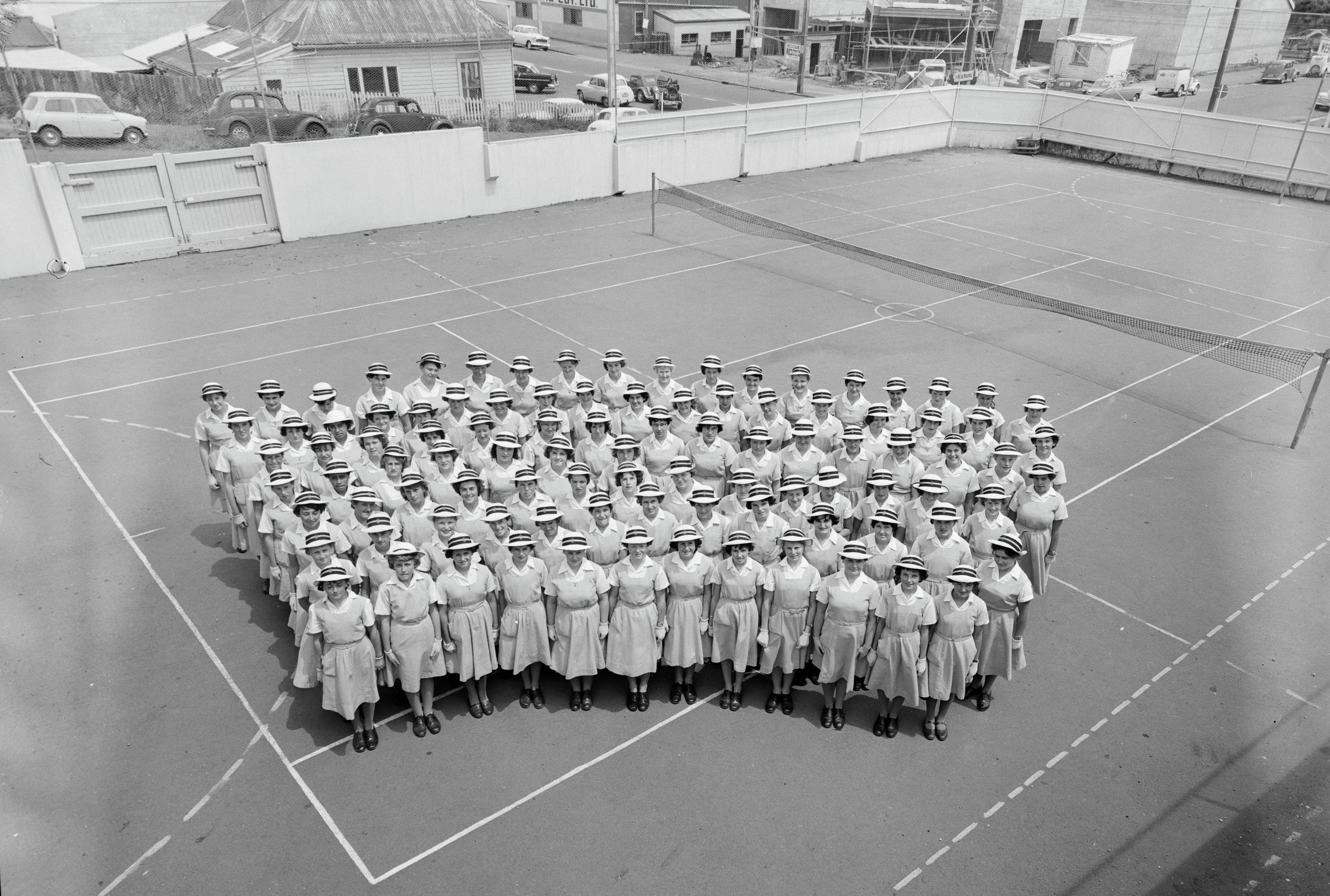 Convent school pupils on the tennis courts at the corner of Powderham and Dawson Streets (7 December 1960). Swainson's Studios. Collection of Puke Ariki (WD.012755).